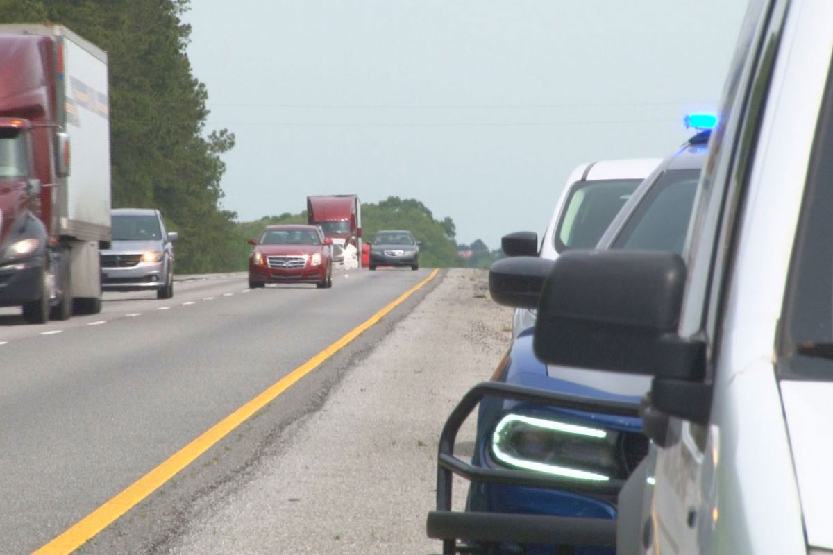 A view of oncoming traffic on a highway with several cars and a police car pulled over on the shoulder.