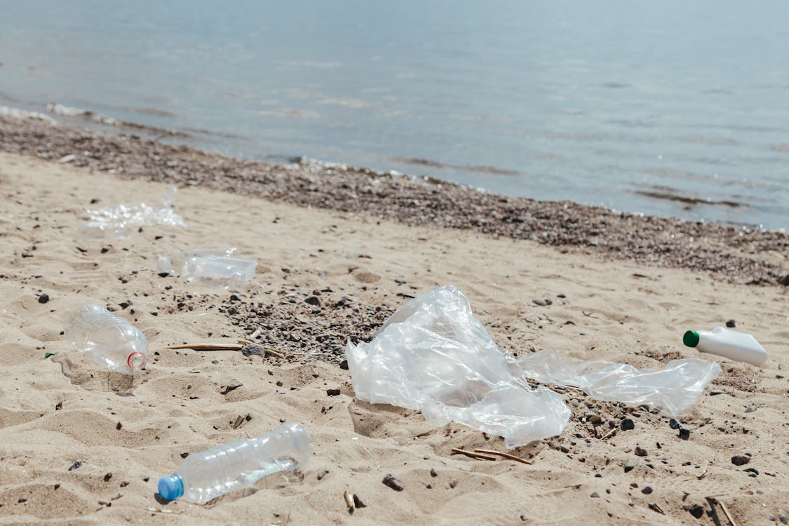 Plastic bags and plastic bottles on sand near a water shore.